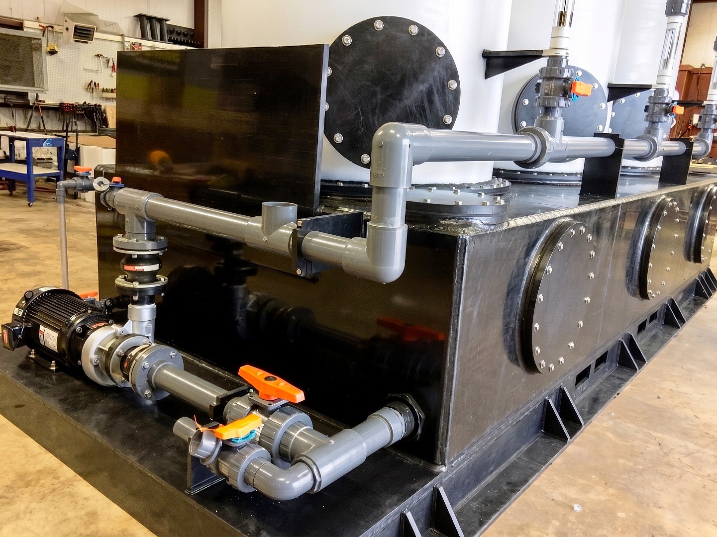 Black industrial manifold system with multiple bolted flanges, grey PVC pipes, and orange-handled valves