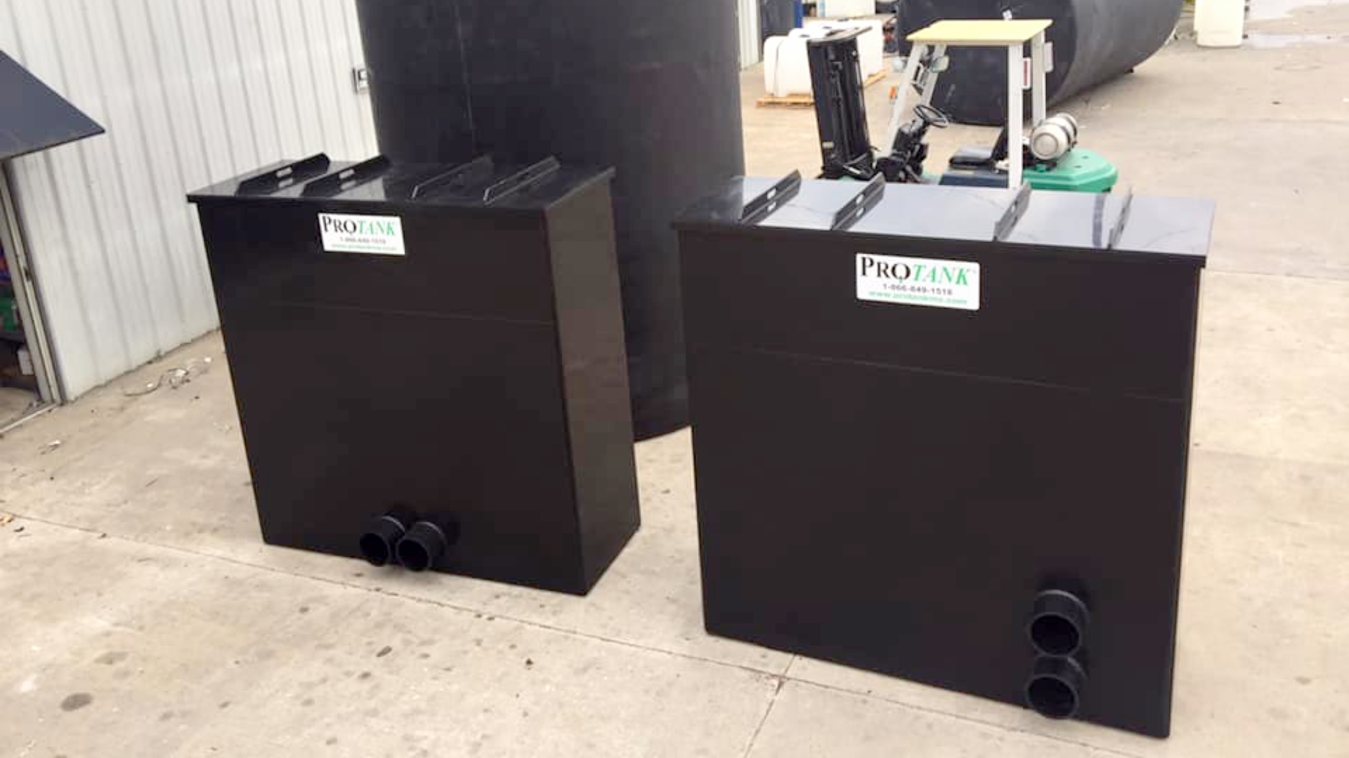 Two identical black rectangular storage tanks with bottom pipe outlets and recessed lids, designed for space-efficient industrial chemical storage