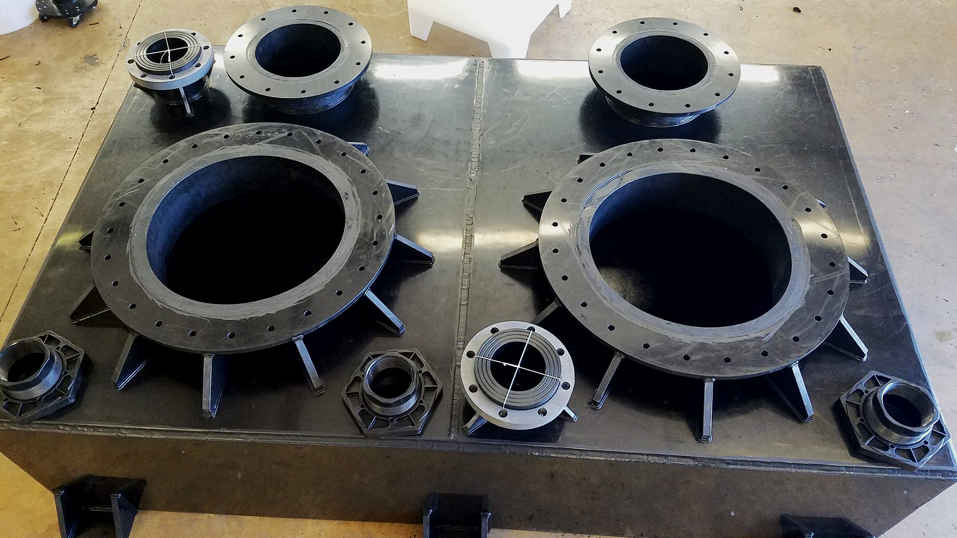 Top view of an industrial storage tank deck with a symmetrical layout of multiple bolted flange fittings and threaded ports