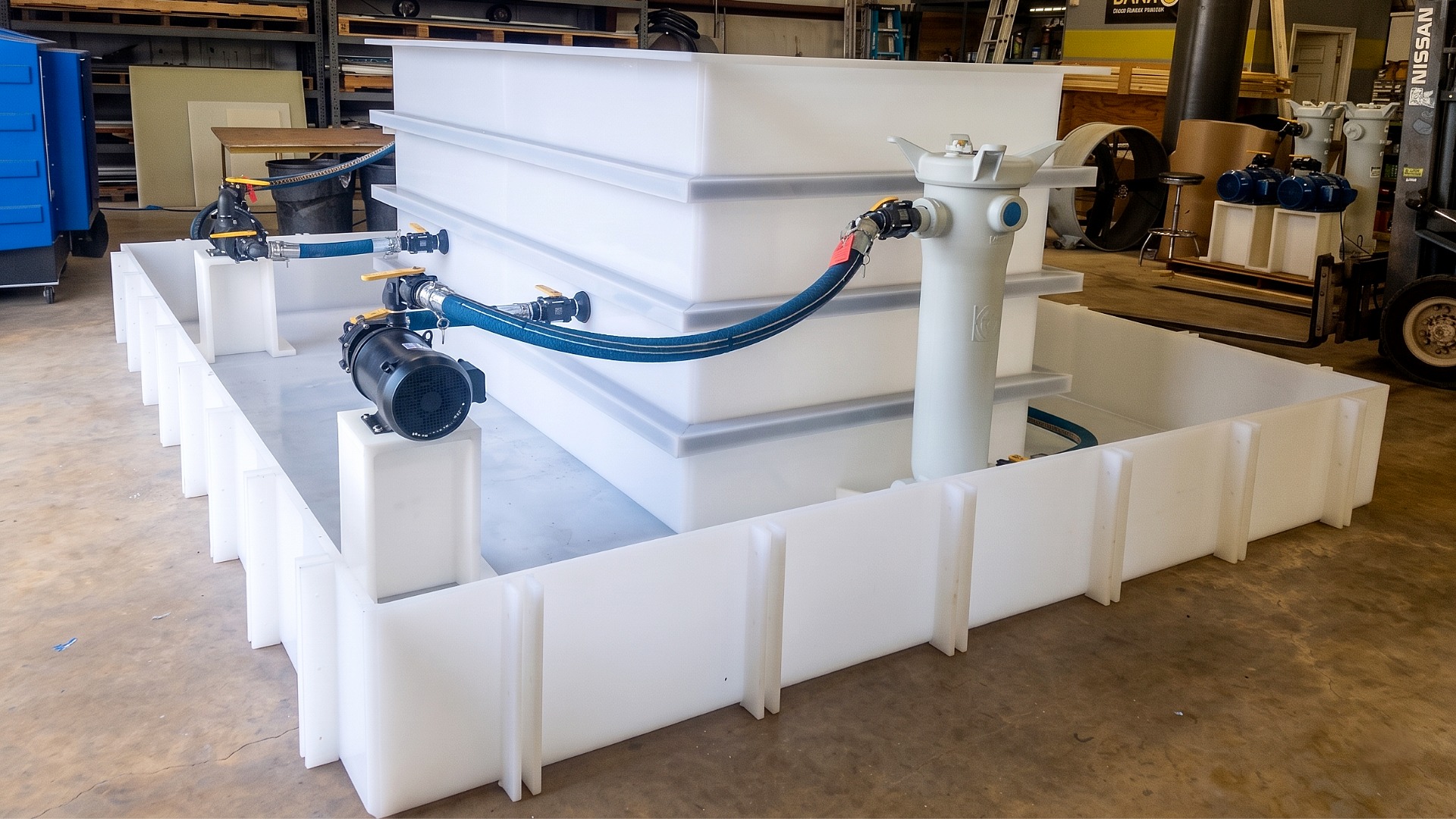 A custom plastic processing system with a central rectangular tank, external filter housing, and electric pump all in a secondary containment basin