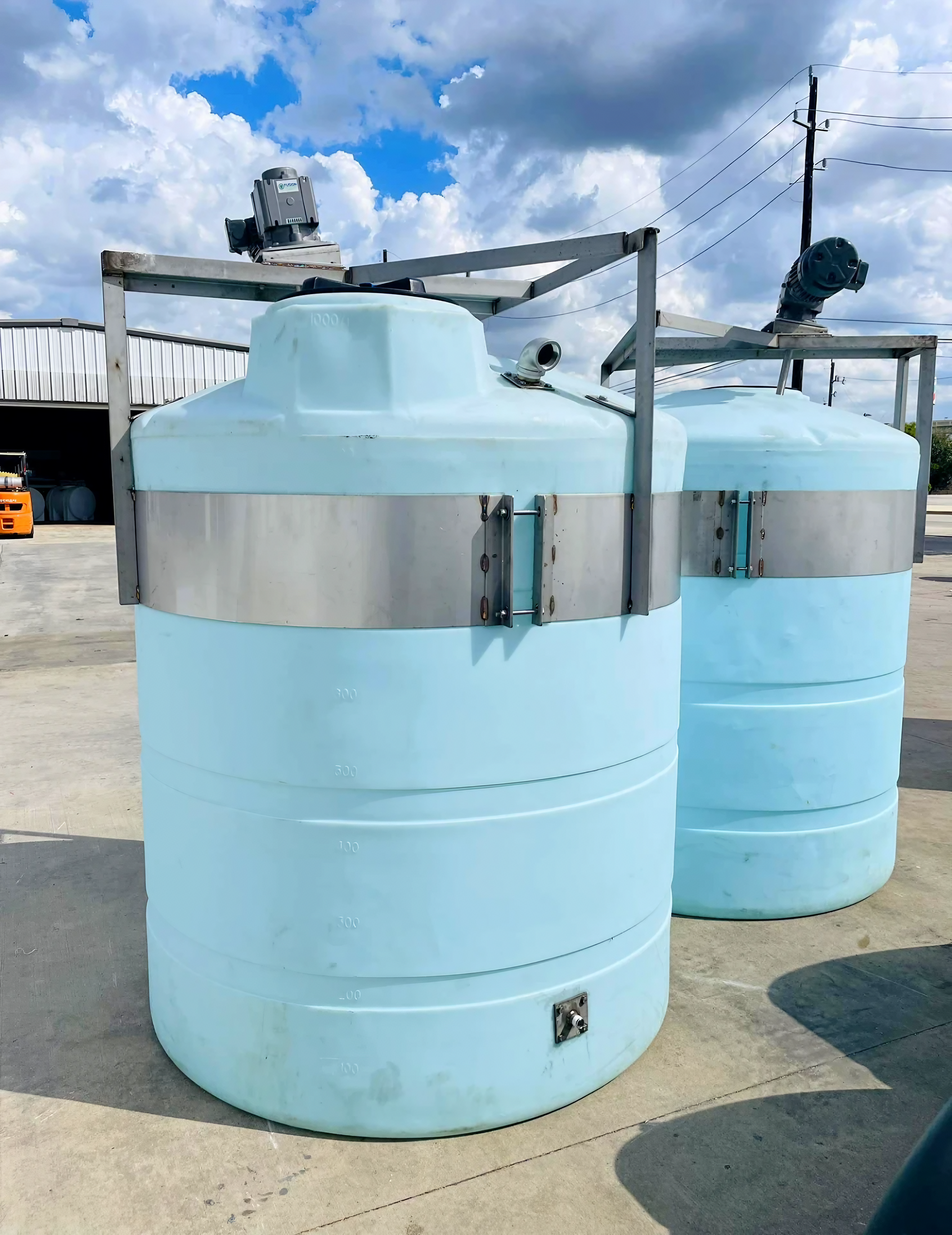 Two vertical polyethylene tanks with steel reinforcement bands and top mounted mixers for industrial agitation and blending