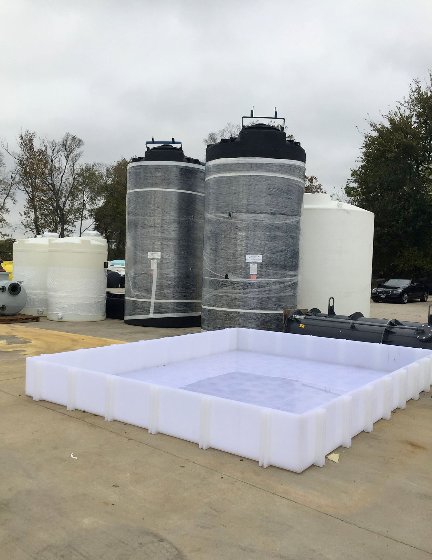 A large rectangular polypropylene secondary containment basin staged outdoors near several large vertical tanks