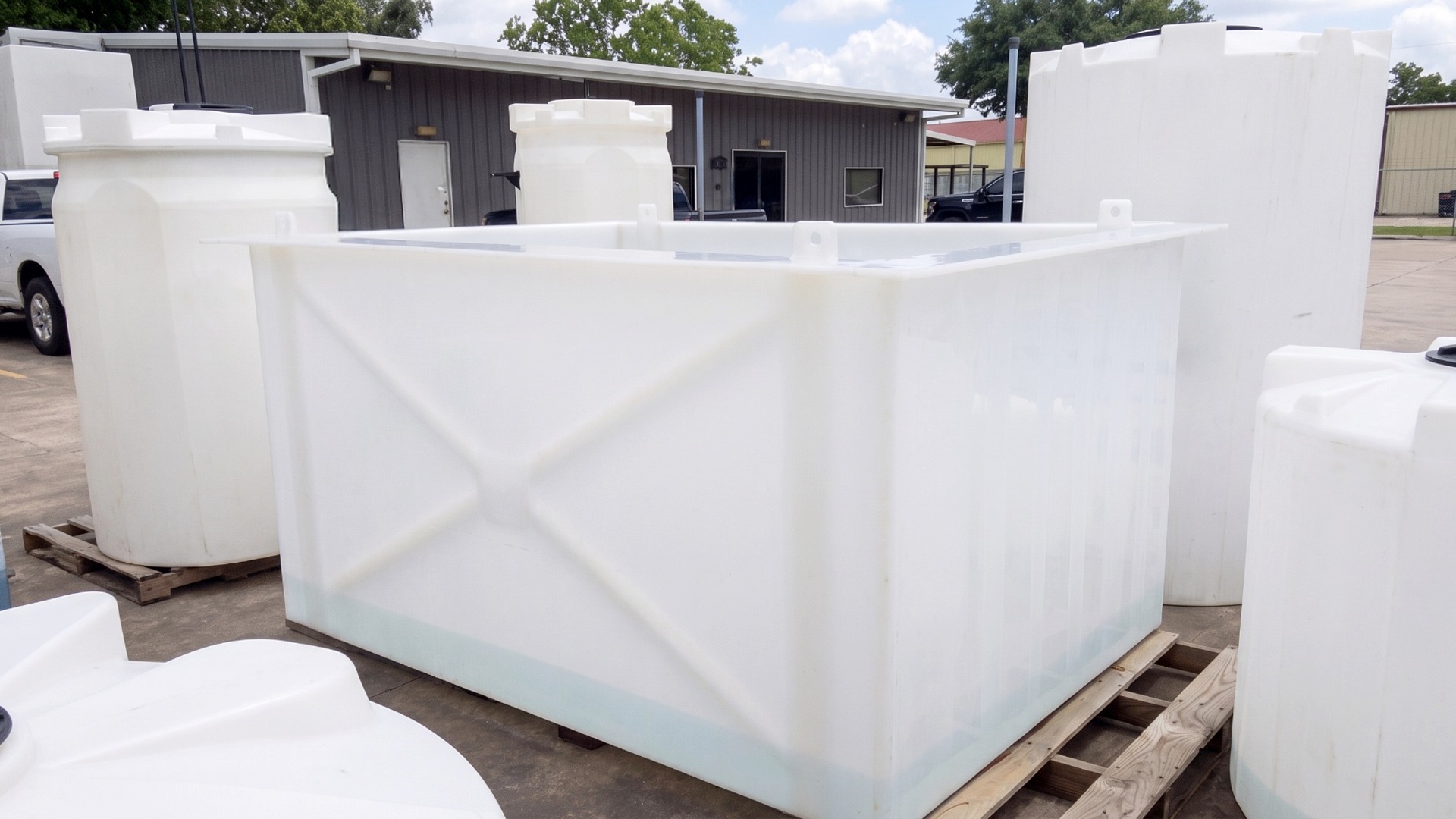 An image showing a custom, open top polypropylene tank with lifting lugs and sidewall reinforcements next to other poly tanks in a business yard
