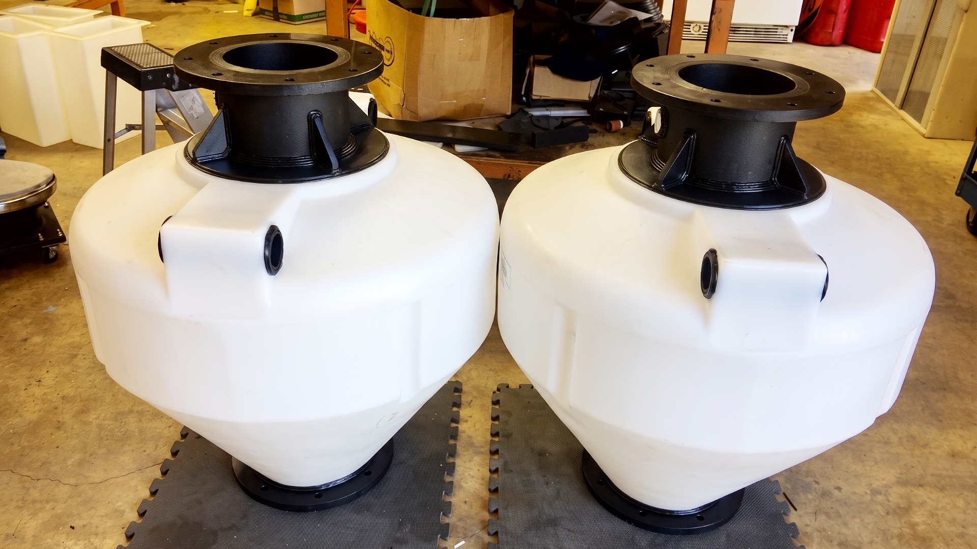 Two white polyethylene cone bottom tanks modified with heavy duty black flange fittings and top access ports
