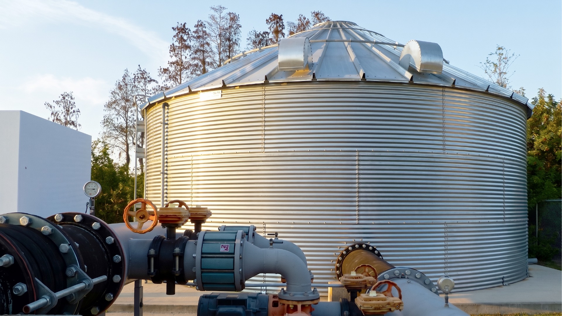 A closeup image of a galvanized steel water tank used for emergency water reserve and supply showing a high volume, multifaceted plumbing manifold attached to the tank