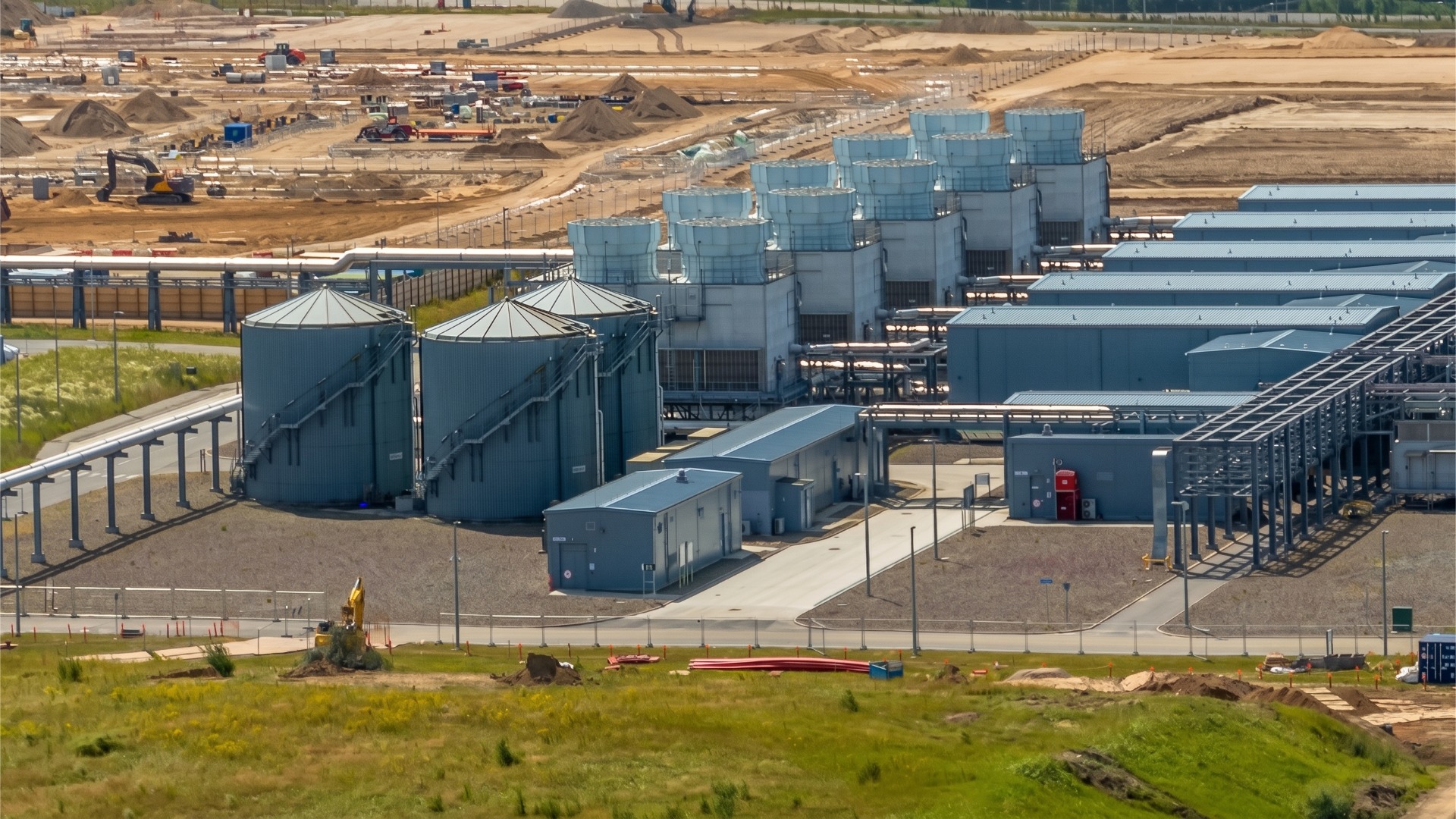 A far out image of a data center facility under construction showcasing an external evaporative cooling system with three, concurrently maintainable, steel emergency water reserve makeup tanks