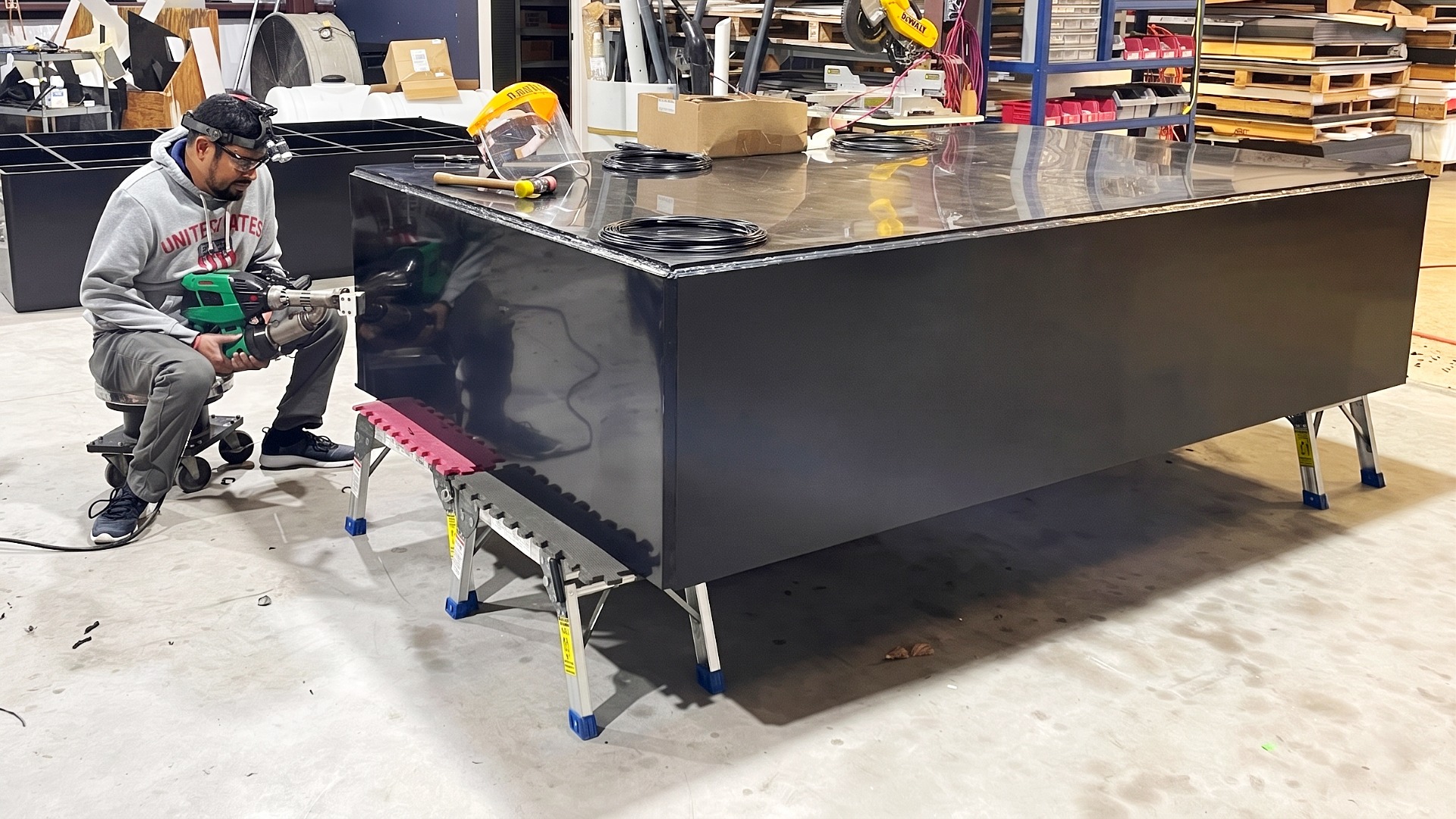 A technician using hand-held extrusion welder to seal the seams of a large black rectangular HDPE tank