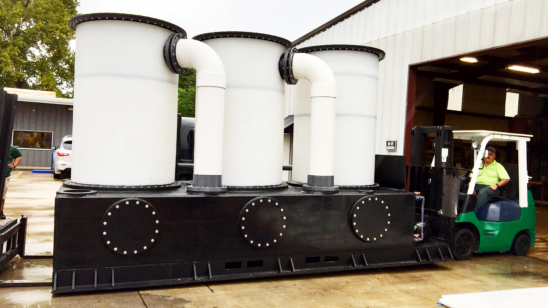 An industrial chemical fume scrubber system with a large base and three tall vertical towers interconnected by PVC piping elbows