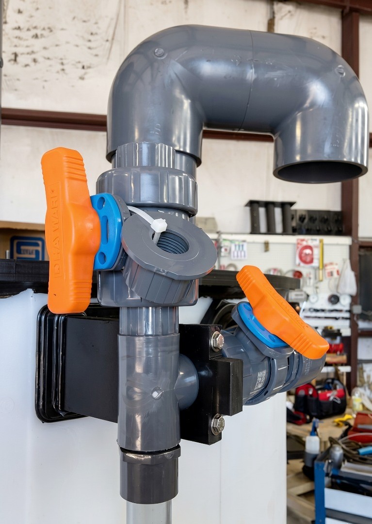 Close-up of grey PVC industrial plumbing with heavy-duty ball valves custom mounted on a white storage tank