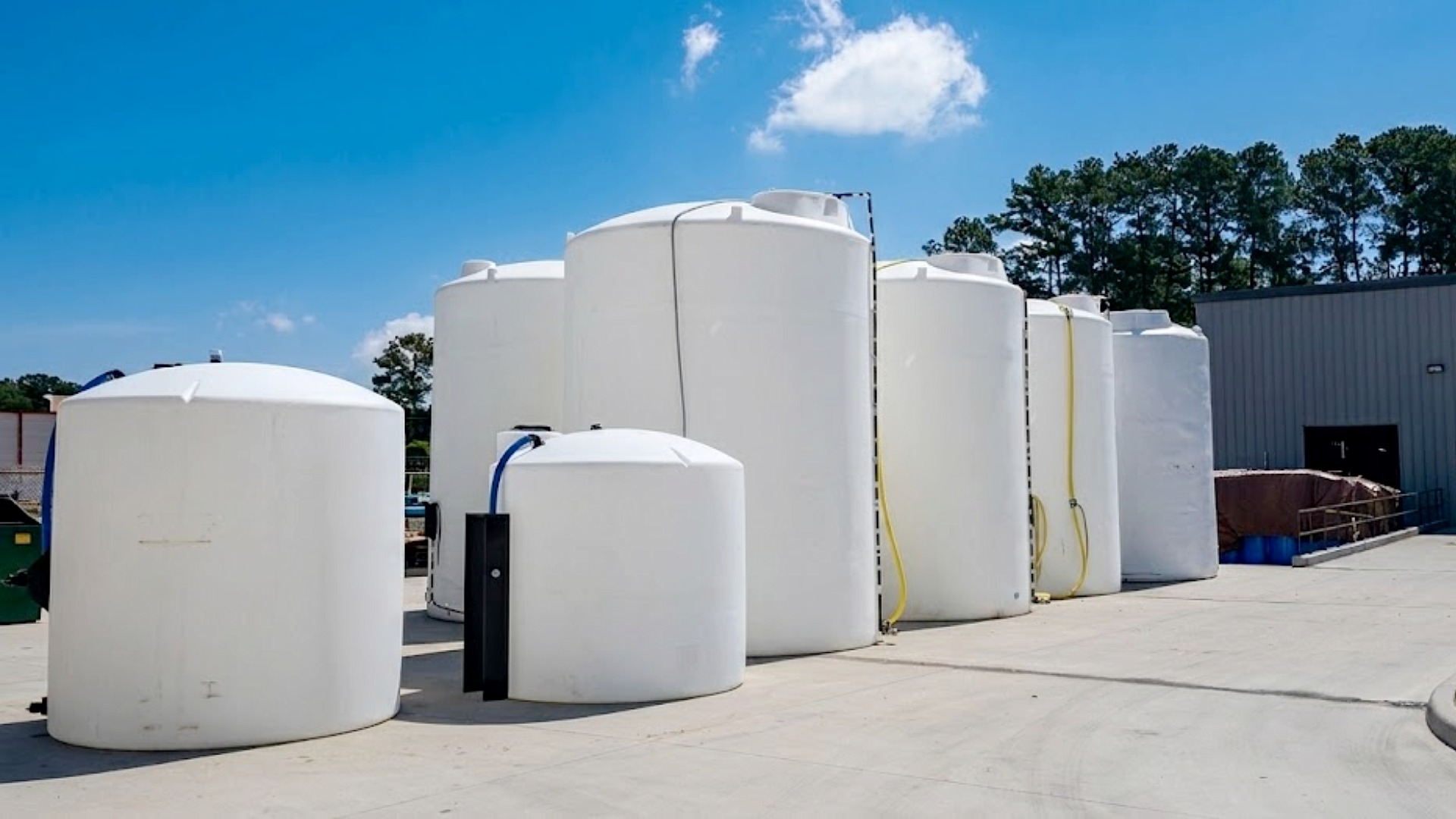 A row of large white vertical polyethylene storage tanks of varying sizes arranged at an industrial site