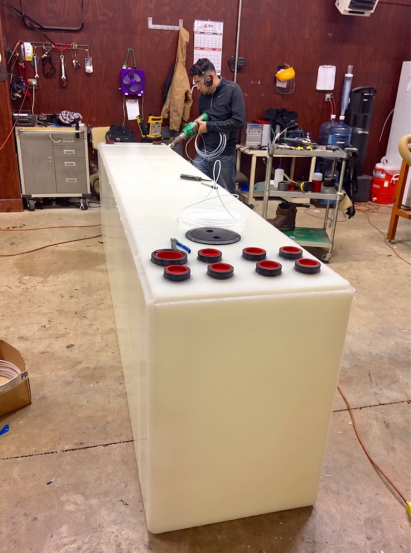 A fabrication specialist using a plastic welding tool to seal the seams of a custom rectangular tank with multiple port fittings