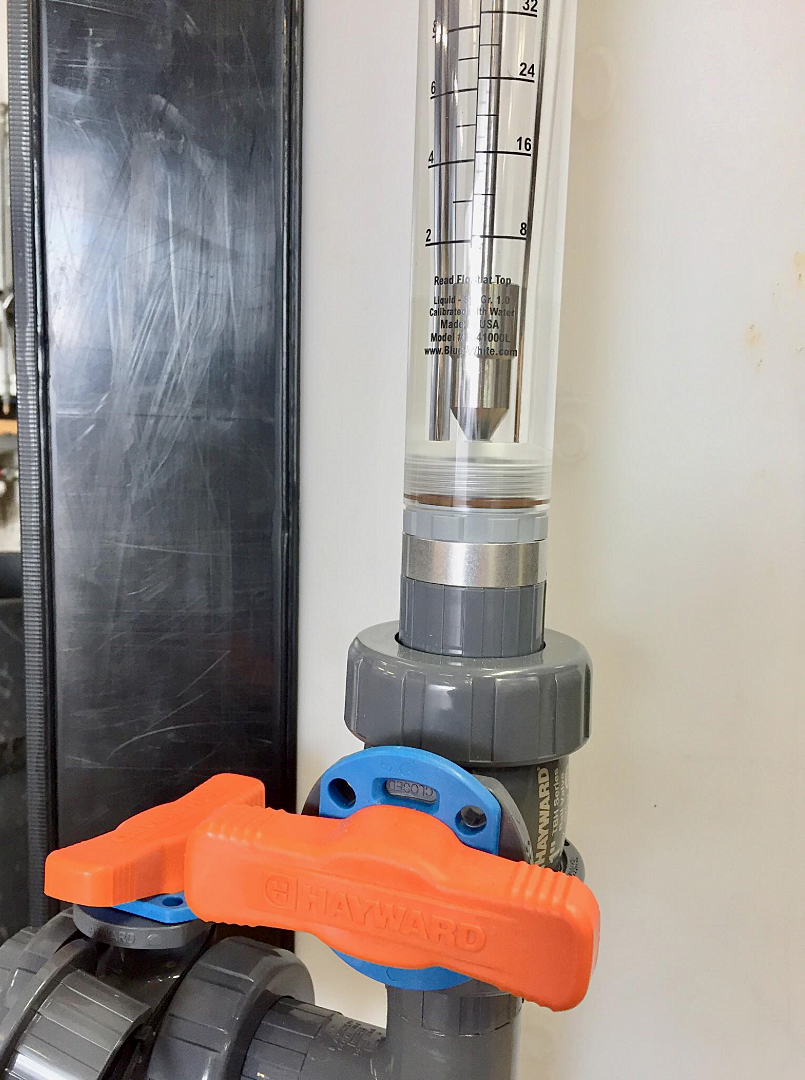 Close-up view of an industrial flow meter scale integrated into a tank's plumbing system above a ball valve
