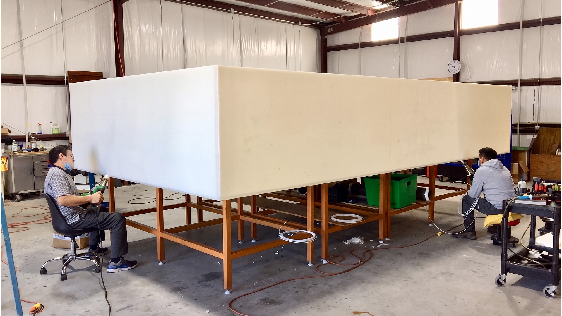 An in-facility image of two Protank fabrication workers extrusion welding a large, rectangular polypropylene tank elevated on worktables