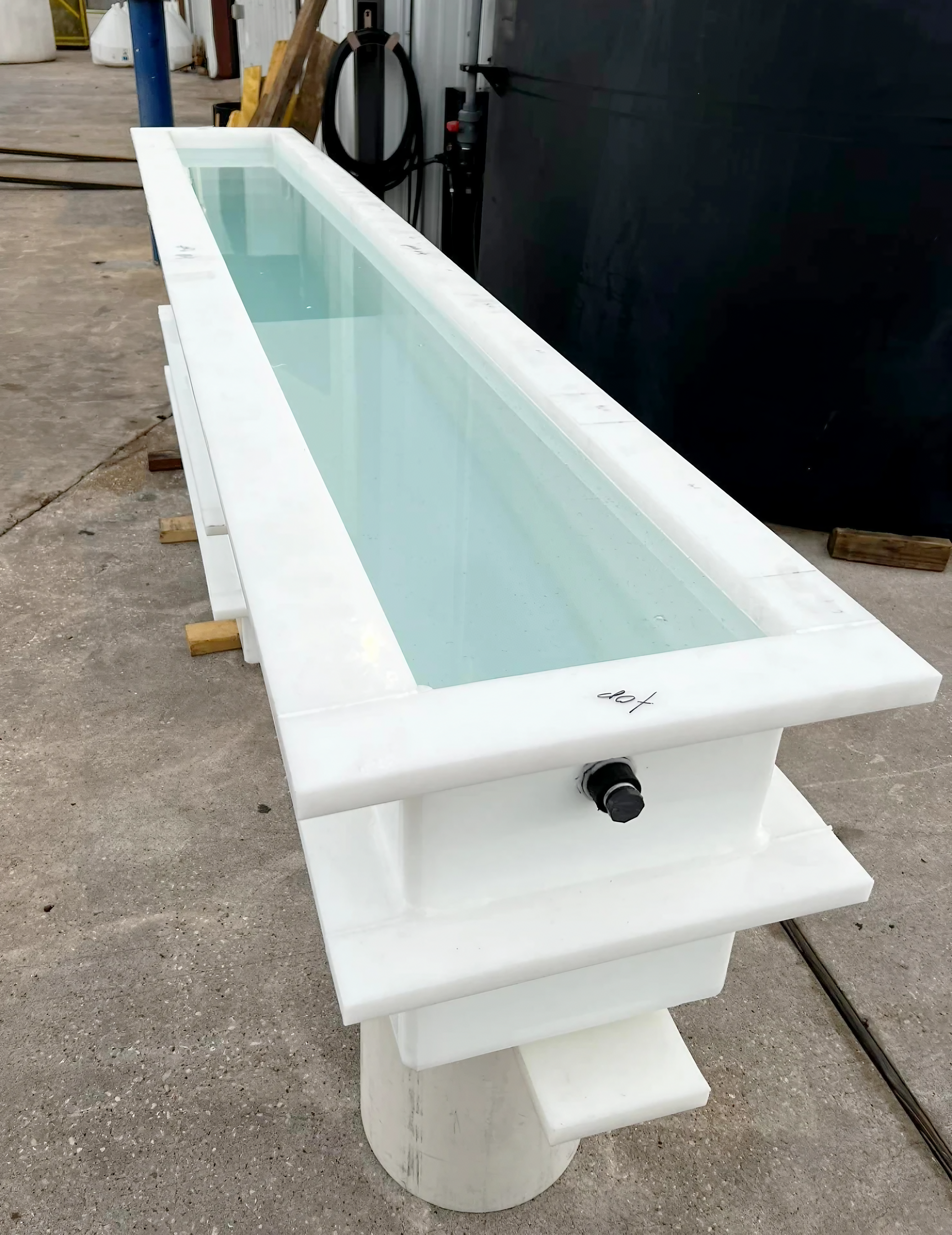 A front view of a long, narrow white custom made polypropylene rinse and dip tank filled with water for testing