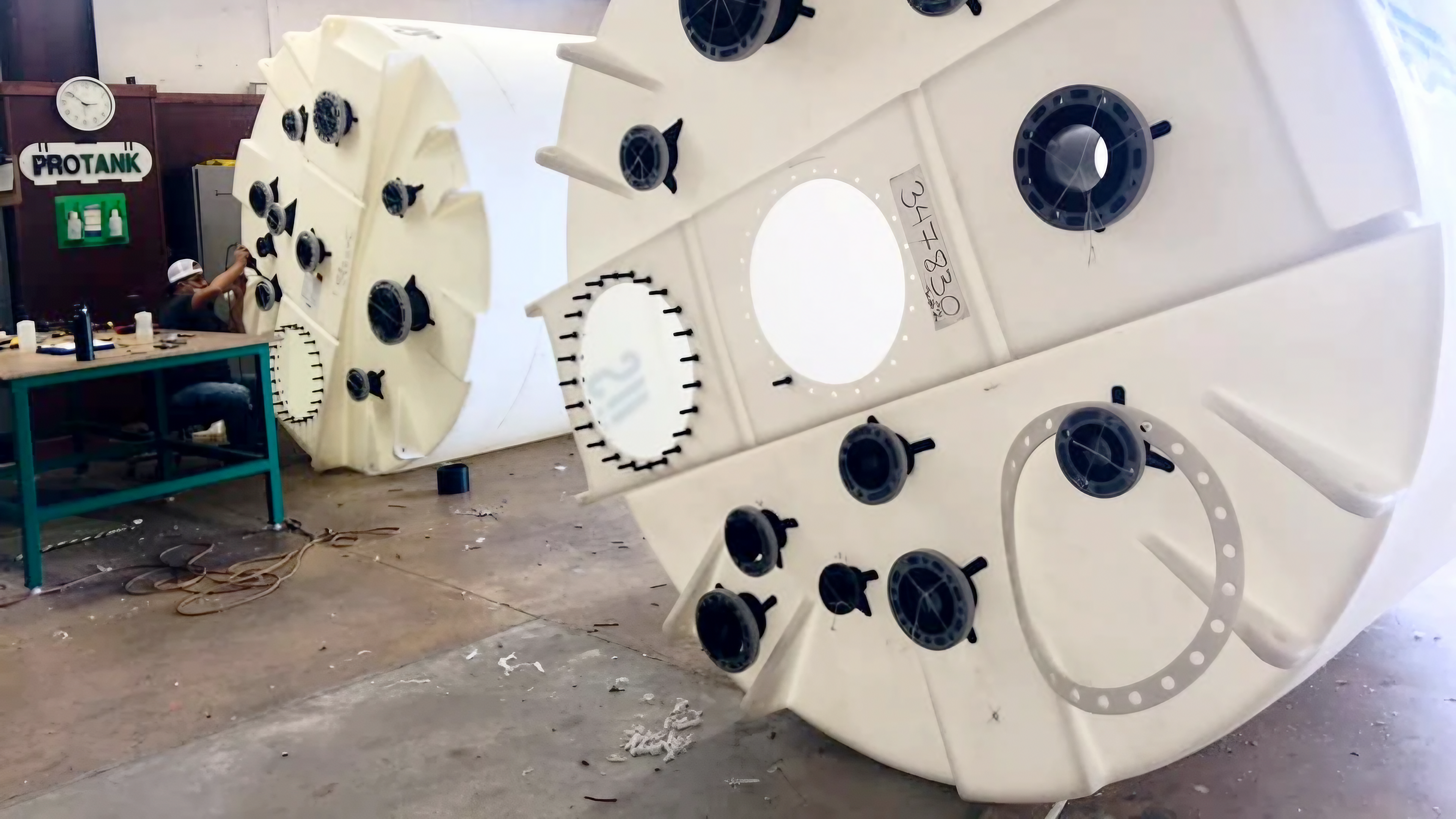 Two large industrial storage tanks undergoing custom outfitting in a workshop with multiple flange fittings and ports