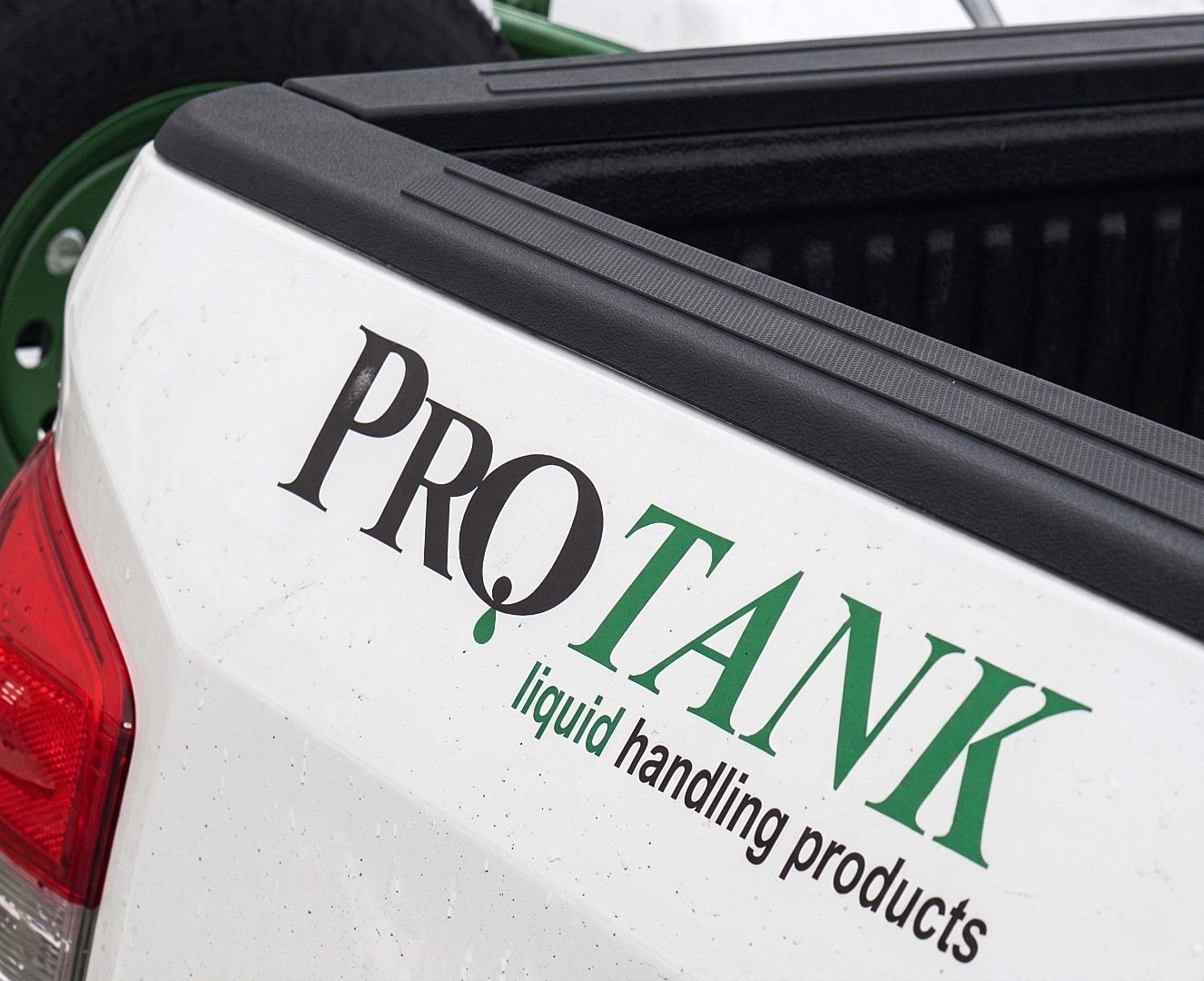 Close-up of the Protank logo in black and green on the corner of a white pickup truck tailgate