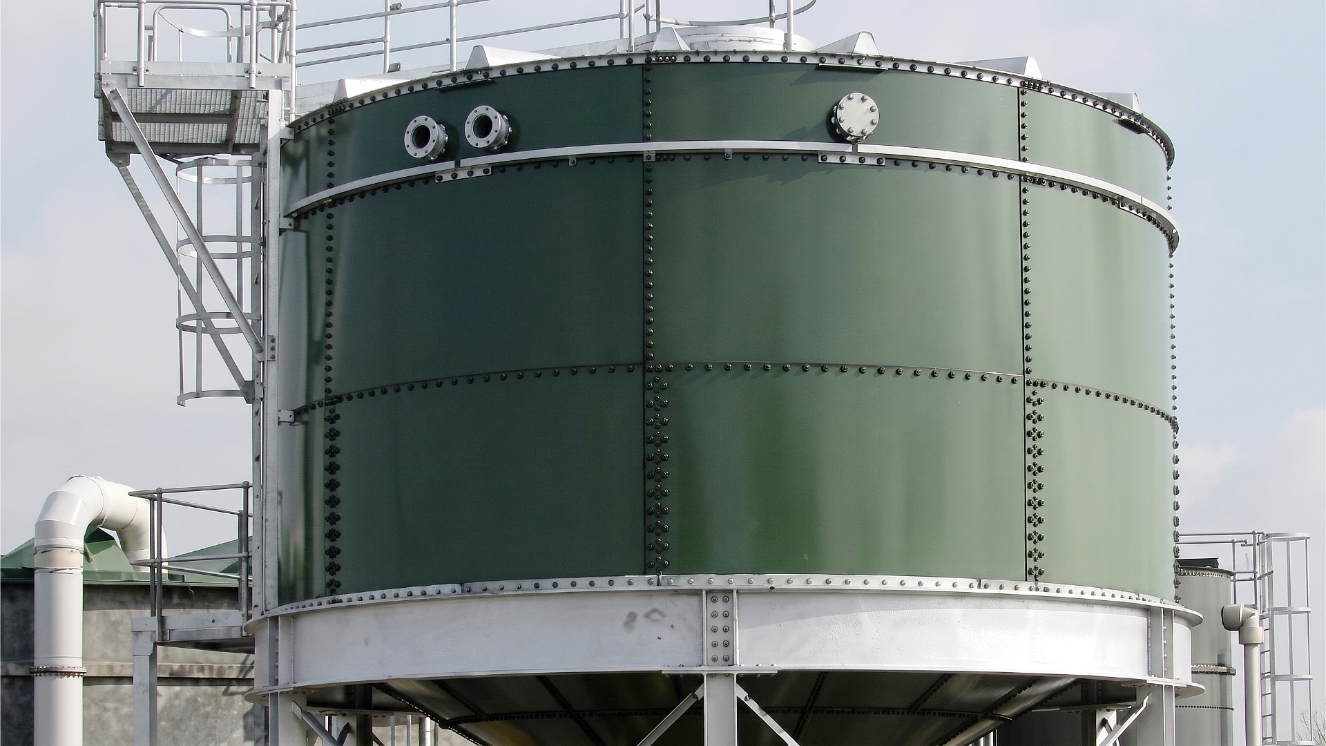 A closeup image of a green, steel emergency water reserve tank with safety ladder installed on the roof of a building for gravity feed and improved water pressure