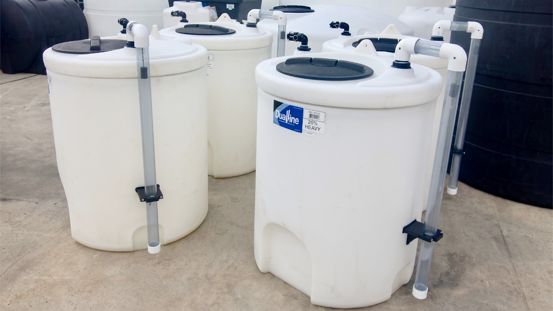 A group of small-capacity polyethylene tanks with clear external dip tubes and PVC manifold fittings
