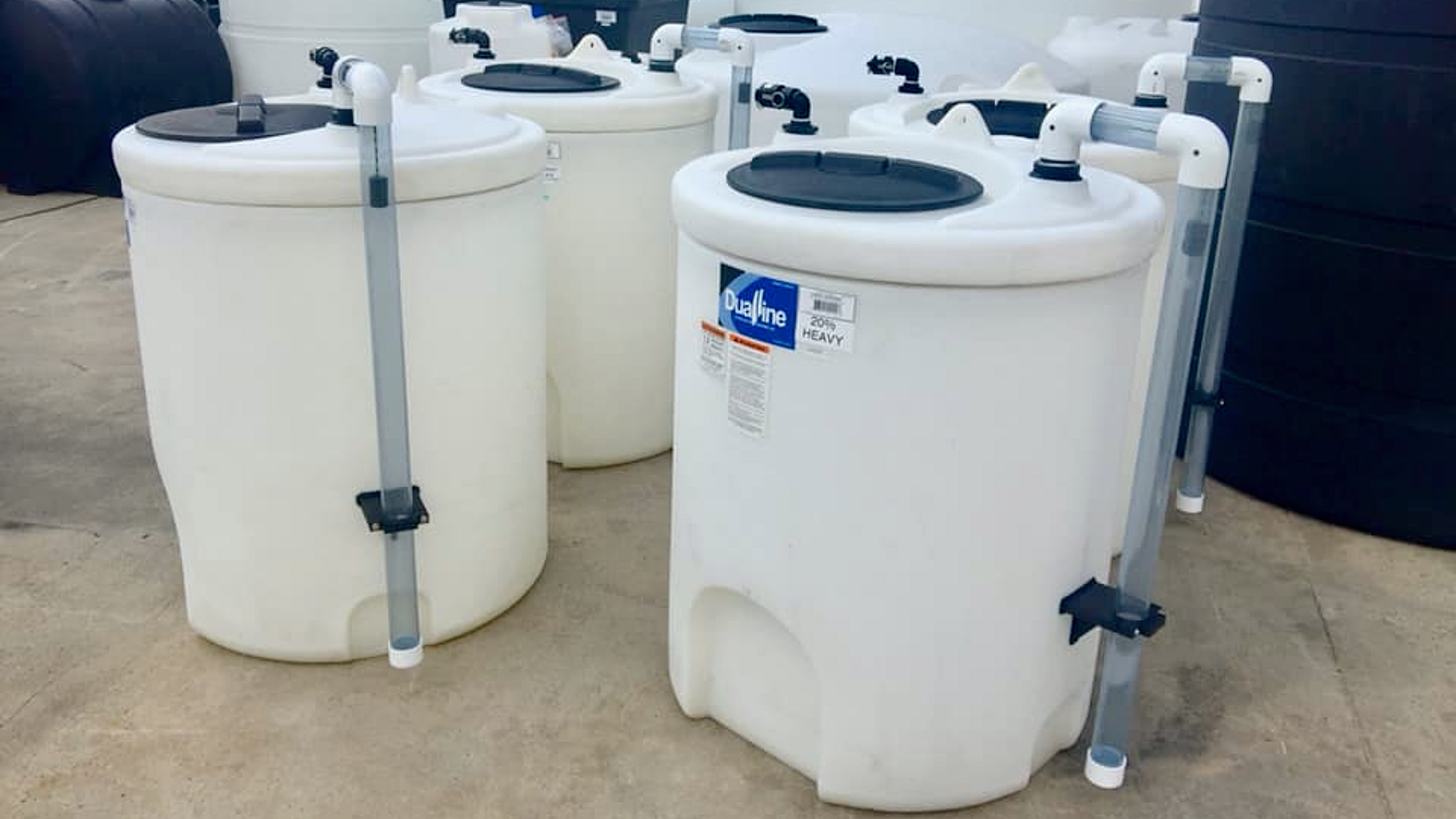 A group of small-capacity polyethylene tanks with clear external dip tubes and PVC manifold fittings